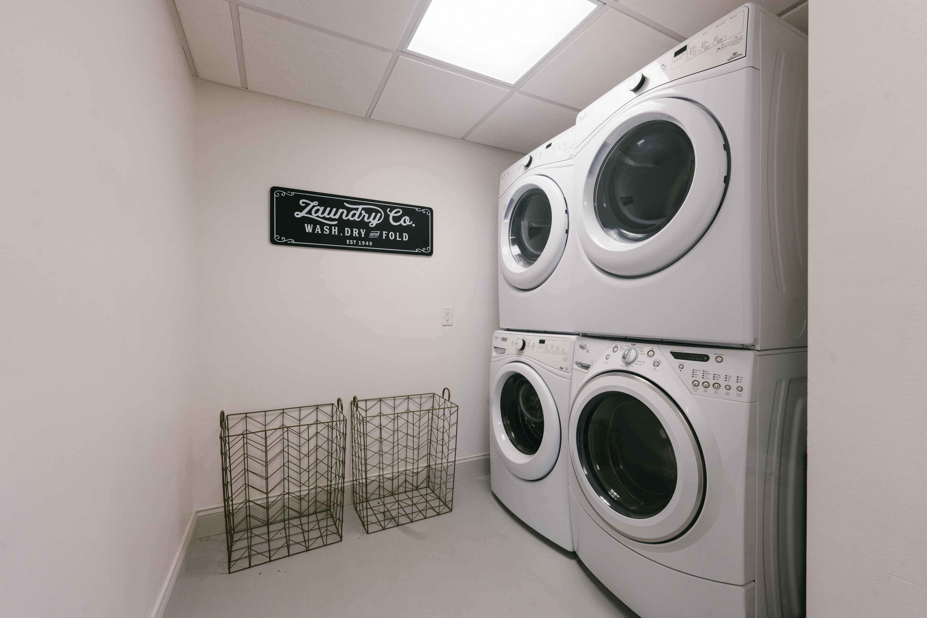 A laundry room with two stacked front-loading washing machines and a sign that reads "Laundry Co. Wash, Dry, Fold."