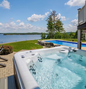 A hot tub with a view of a lake, surrounded by a deck and a lounge chair. -  ADIRONDACK LUXURY LAKE ESTATE: POOL & HOT TUB! NEWLY RENOVATED! (Remsen)