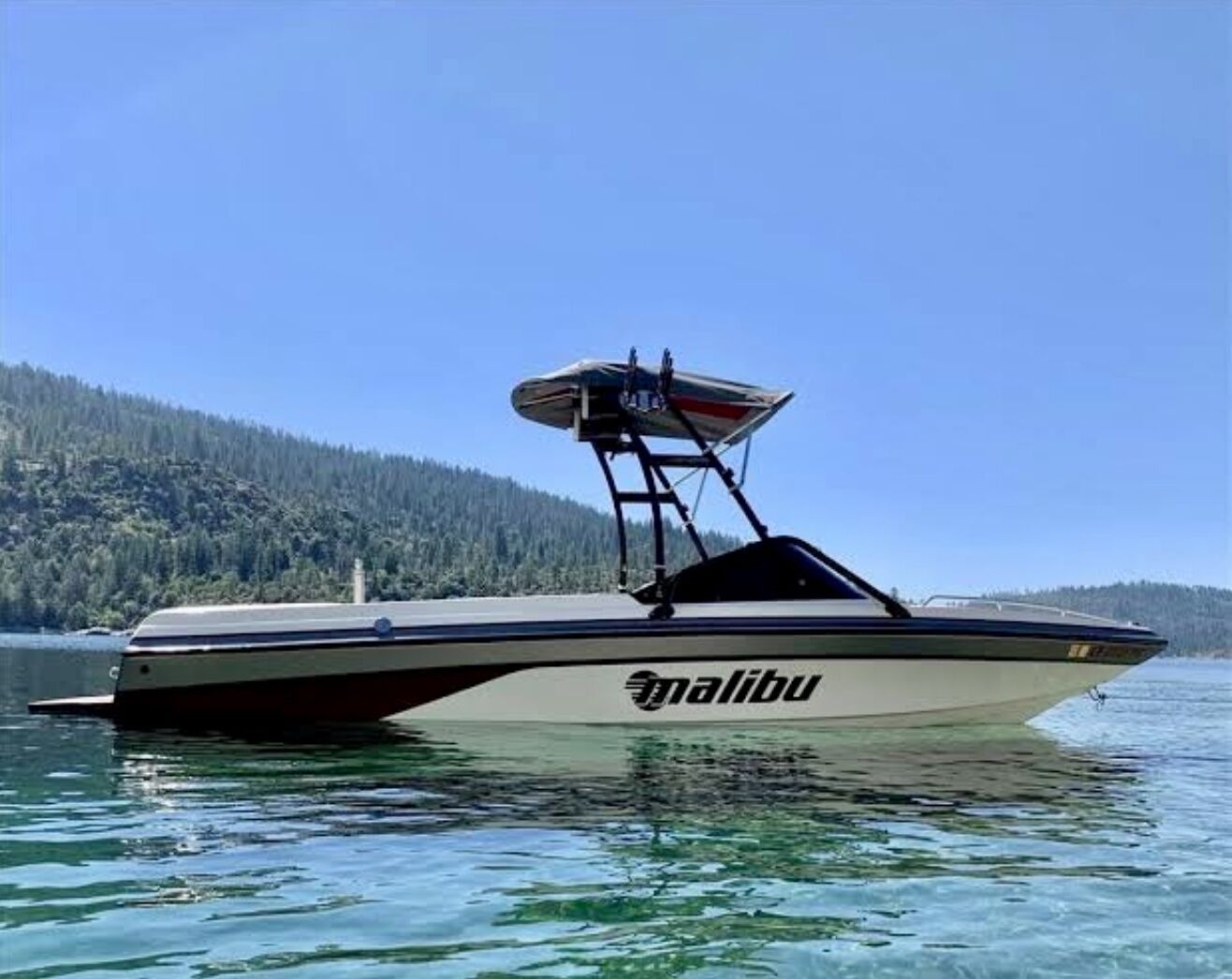 Un lancha rápida en Malibu sobre aguas tranquilas, con una orilla boscosa al fondo.