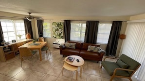 Un salon comprenant un canapé, une table à manger et une table basse. On y trouve également un ventilateur de plafond et une fenêtre avec des rideaux.