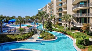 Un complexe hôtelier doté d’une grande piscine, de palmiers et d’un immeuble à plusieurs étages avec des balcons.