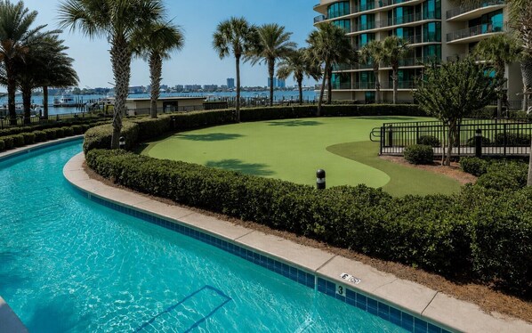 A swimming pool, a golf course, and a modern building with balconies.