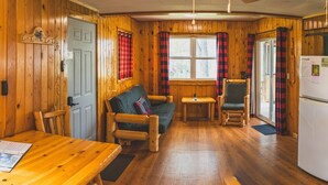 Ein gemütliches Blockhaus-Interieur mit Holzwänden, einem Esstisch, einer Couch, einem Sessel und einem kleinen Tisch.