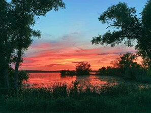 Auringonlasku tyynen järven yllä, ja puut kehystävät maisemaa.
