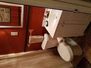 Bathroom features a white toilet, vanity, and mirror, along with a towel rack and artwork.