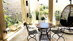 Une terrasse extérieure ensoleillée, avec une table ronde et des chaises, entourée de plantes en pot et agrémentée d’un fauteuil suspendu.