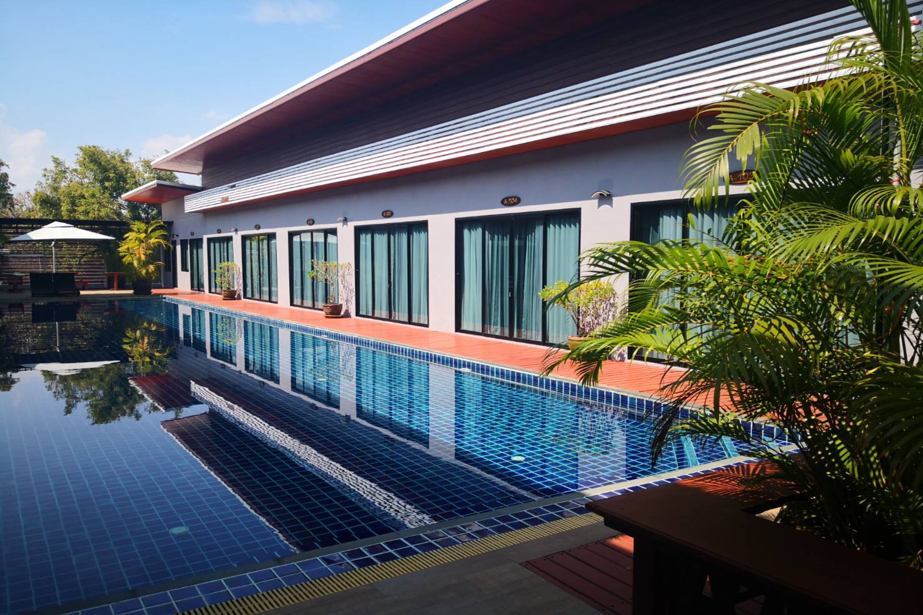 A modern hotel with a swimming pool, large windows, and a red roof.