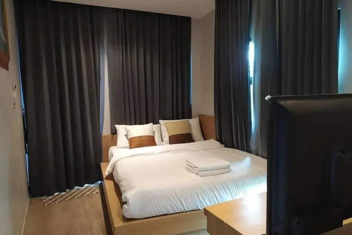 Une chambre d’hôtel moderne avec un grand lit, des rideaux foncés, une table de chevet en bois et un téléviseur.