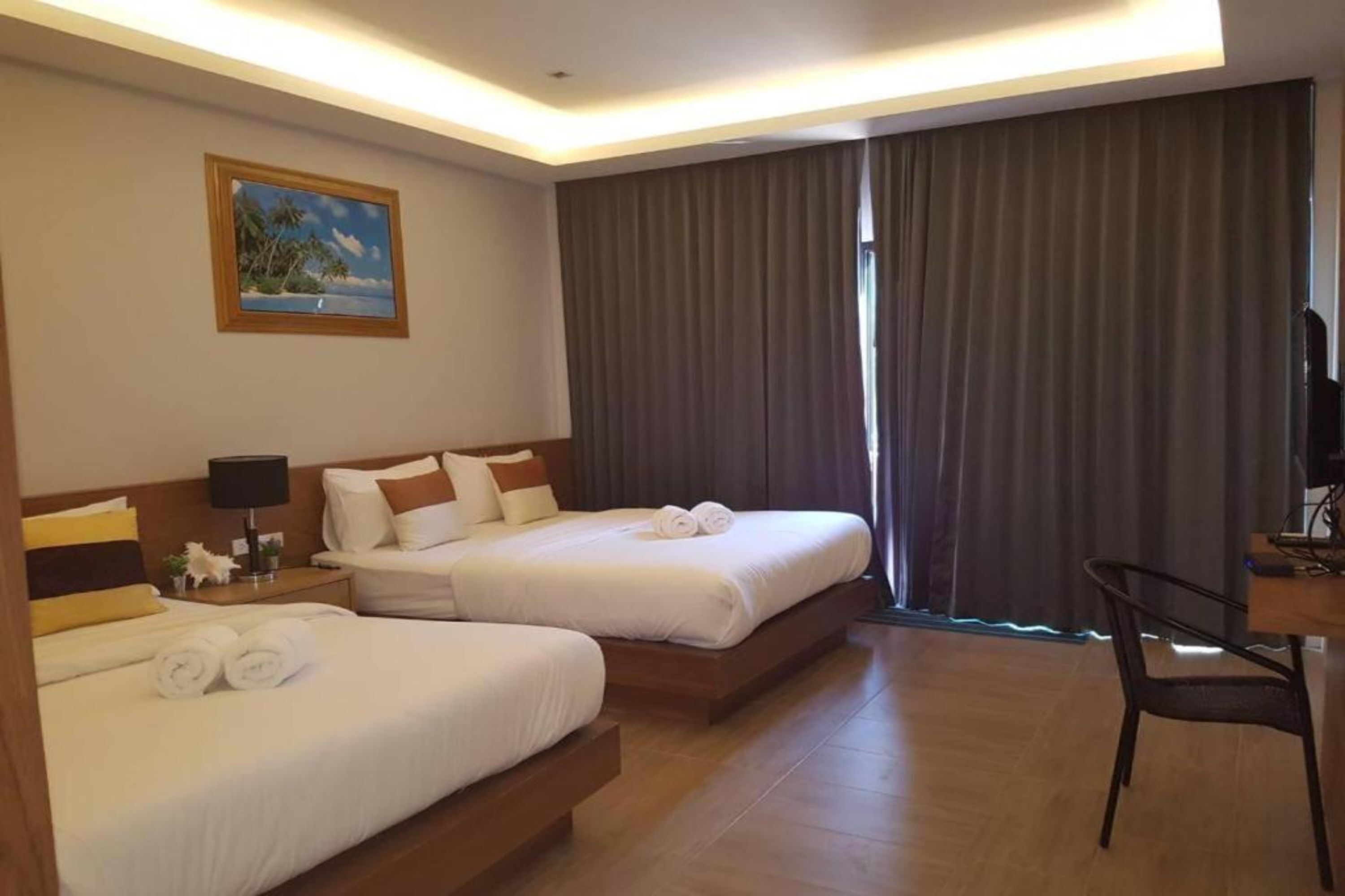 A hotel room with two beds, a desk, a chair, a painting on the wall, and a large window with curtains.
