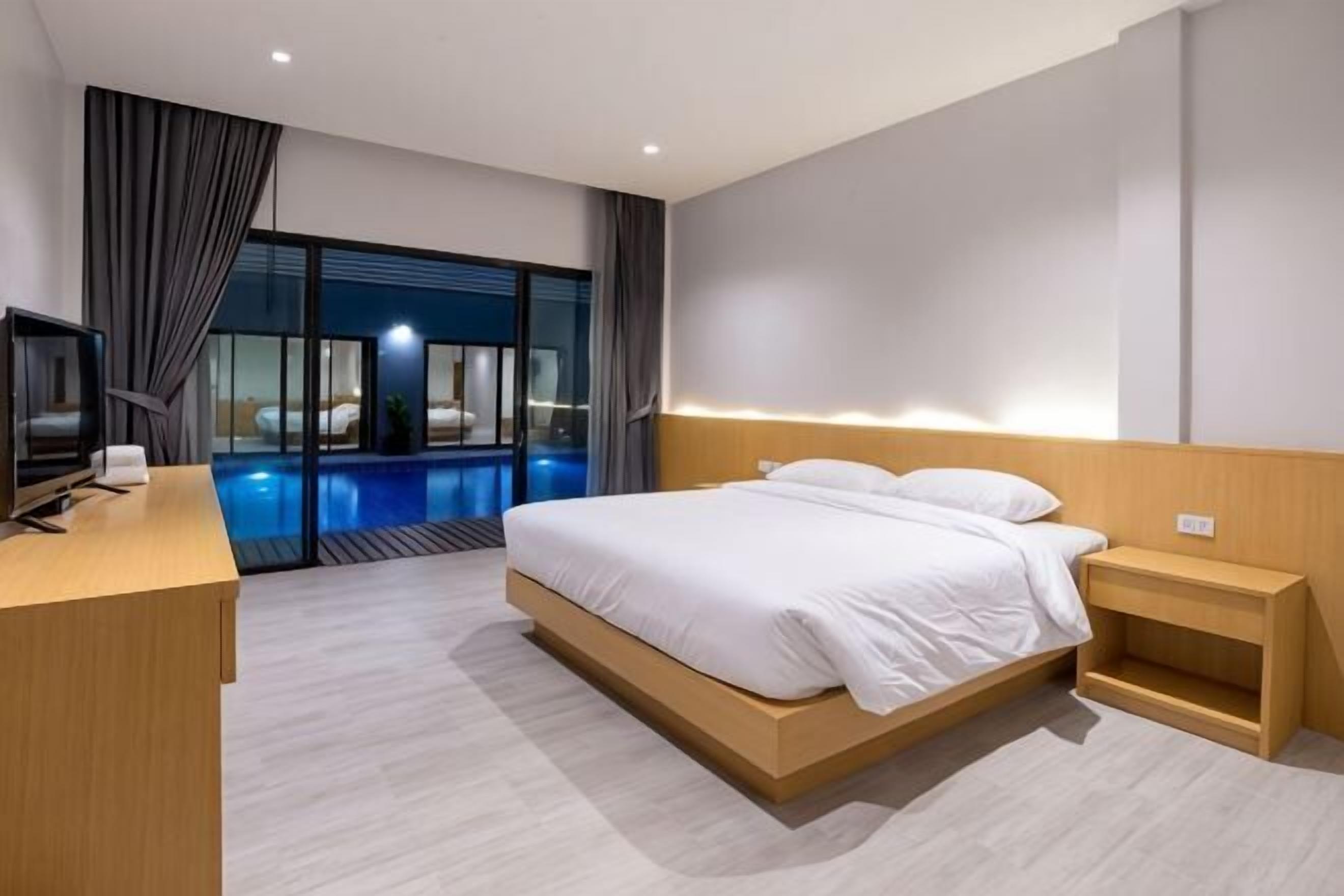 Ein modernes Hotelzimmer mit Bett, Nachttisch, Fernseher und Blick auf einen Außenpool.
