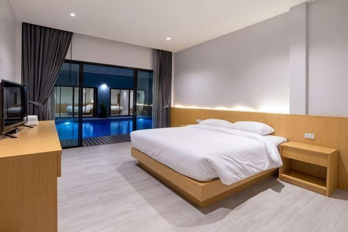 Une chambre d’hôtel moderne équipée d’un lit, d’une table de chevet, d’une télévision et offrant une vue sur une piscine extérieure.