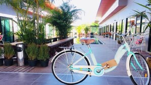 Una bicicleta turquesa estacionada sobre un suelo de baldosas, con plantas en macetas y un banco cerca.