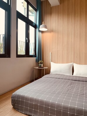 A bedroom with a bed, a bedside table with a plant, a window with curtains, and a hanging light fixture. - OYAJI Guesthouse (Tainan)