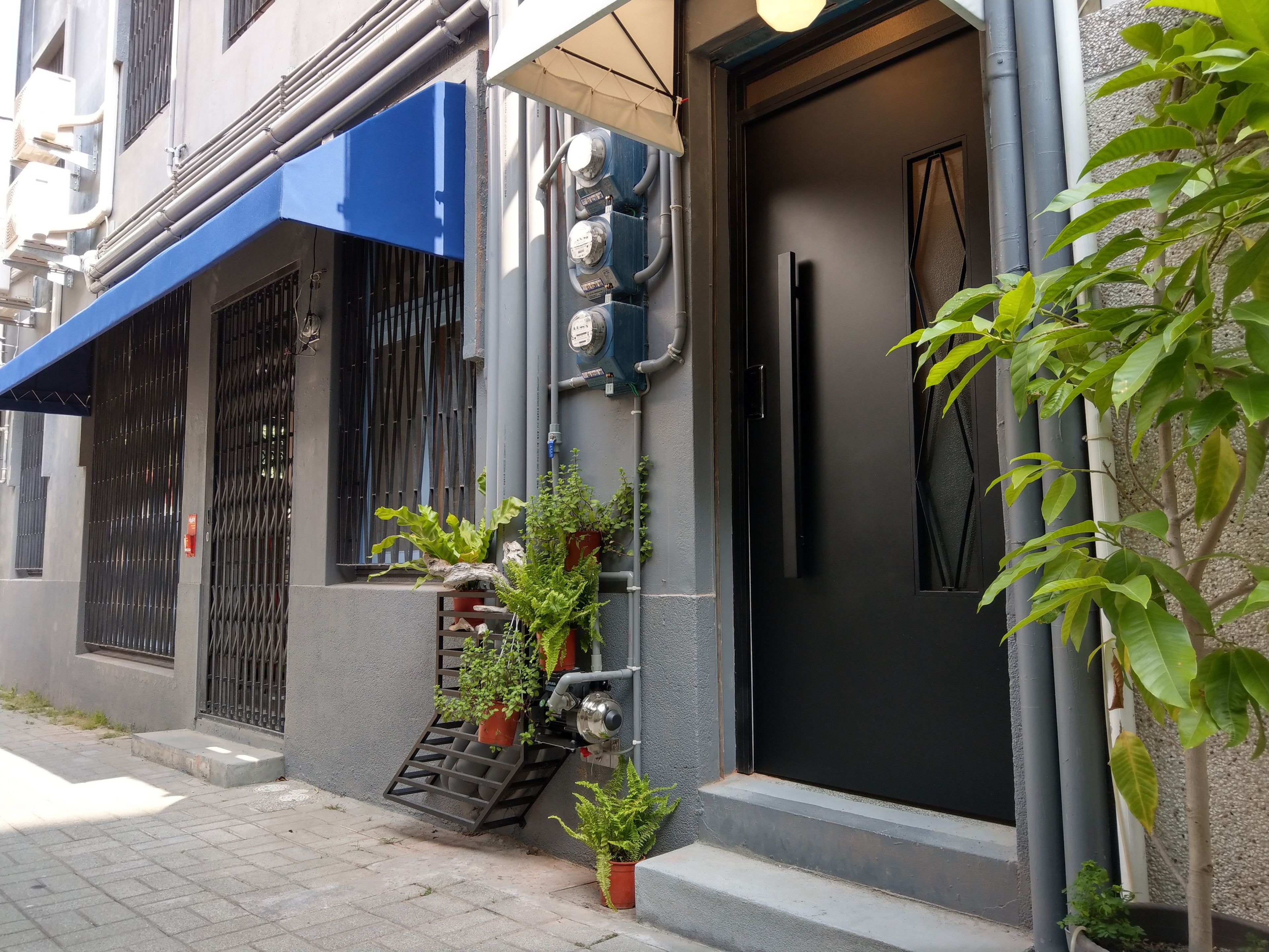 A residential building with a blue awning, a black door, and potted plants on the steps.