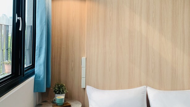 A bedroom with a bed, a small table with a plant, a hanging light, and a window with curtains. - OYAJI Guesthouse (Tainan)