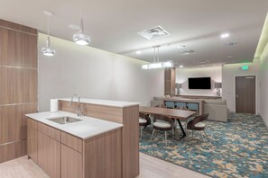 A modern kitchen with a sink, a dining area with chairs, a sofa, and a flat-screen TV.