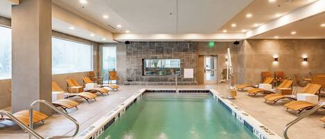 A large indoor swimming pool with multiple lanes, surrounded by lounge chairs and a stone wall.