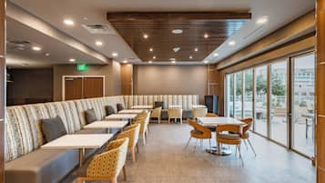 Un restaurant moderne avec un long comptoir, des banquettes et des tables. Un panneau indiquant la sortie est placé au-dessus d’une porte.