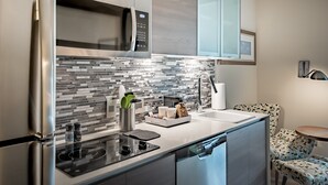 A modern kitchen with stainless steel appliances, a tiled backsplash, and a small dining area with patterned chairs. - Element by Marriott Dallas Downtown East (Dallas)