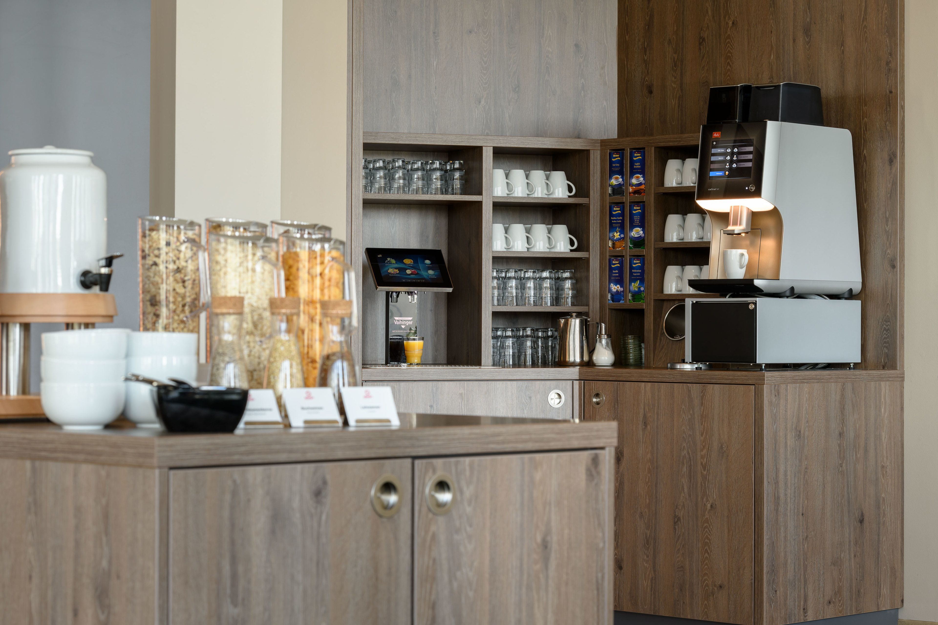 Un espace café moderne comprenant une machine à café, diverses tasses et un présentoir de dosettes de café.