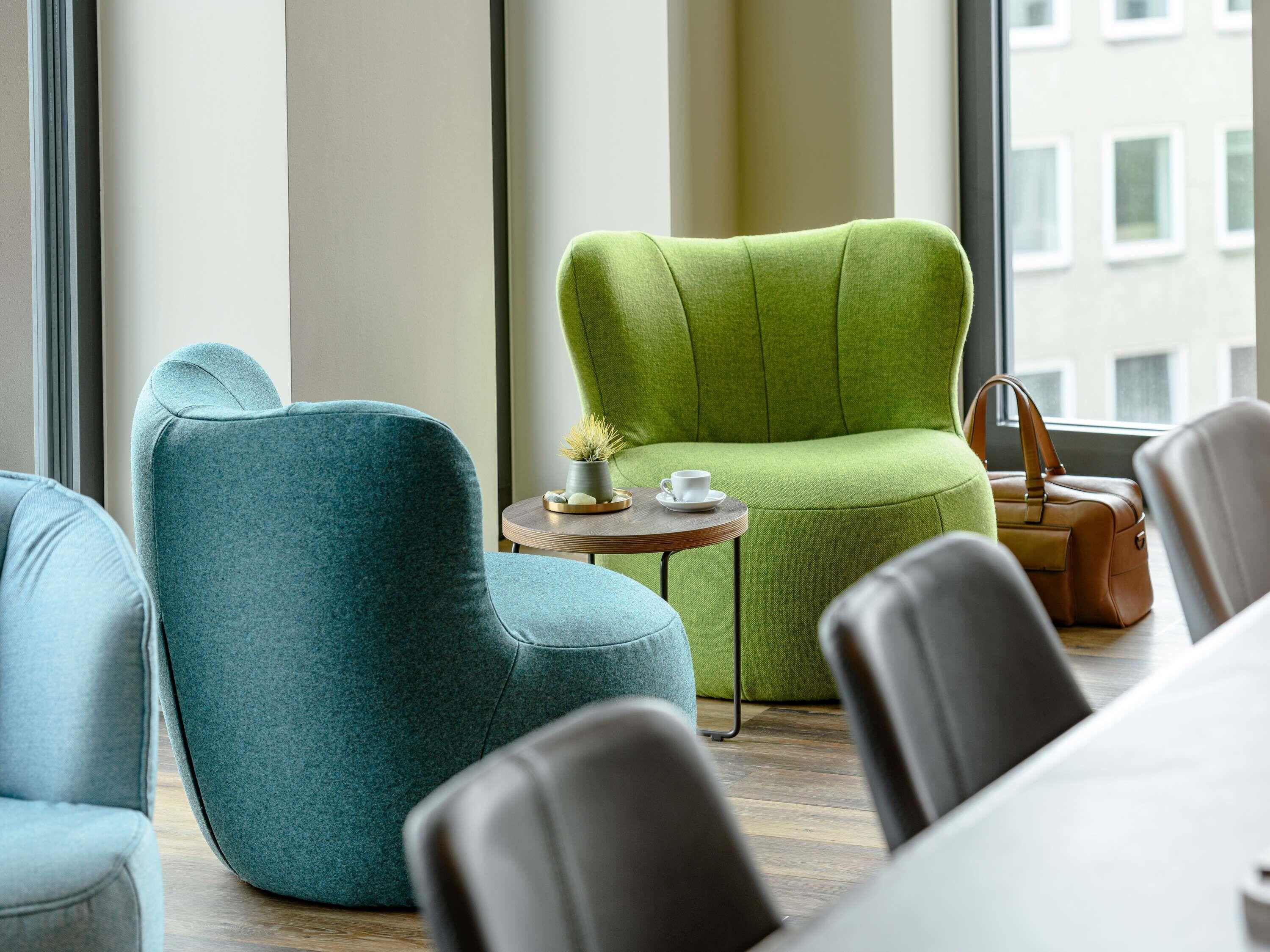 A modern lounge area with seating, a small table with a cup and saucer, and a handbag on the floor.