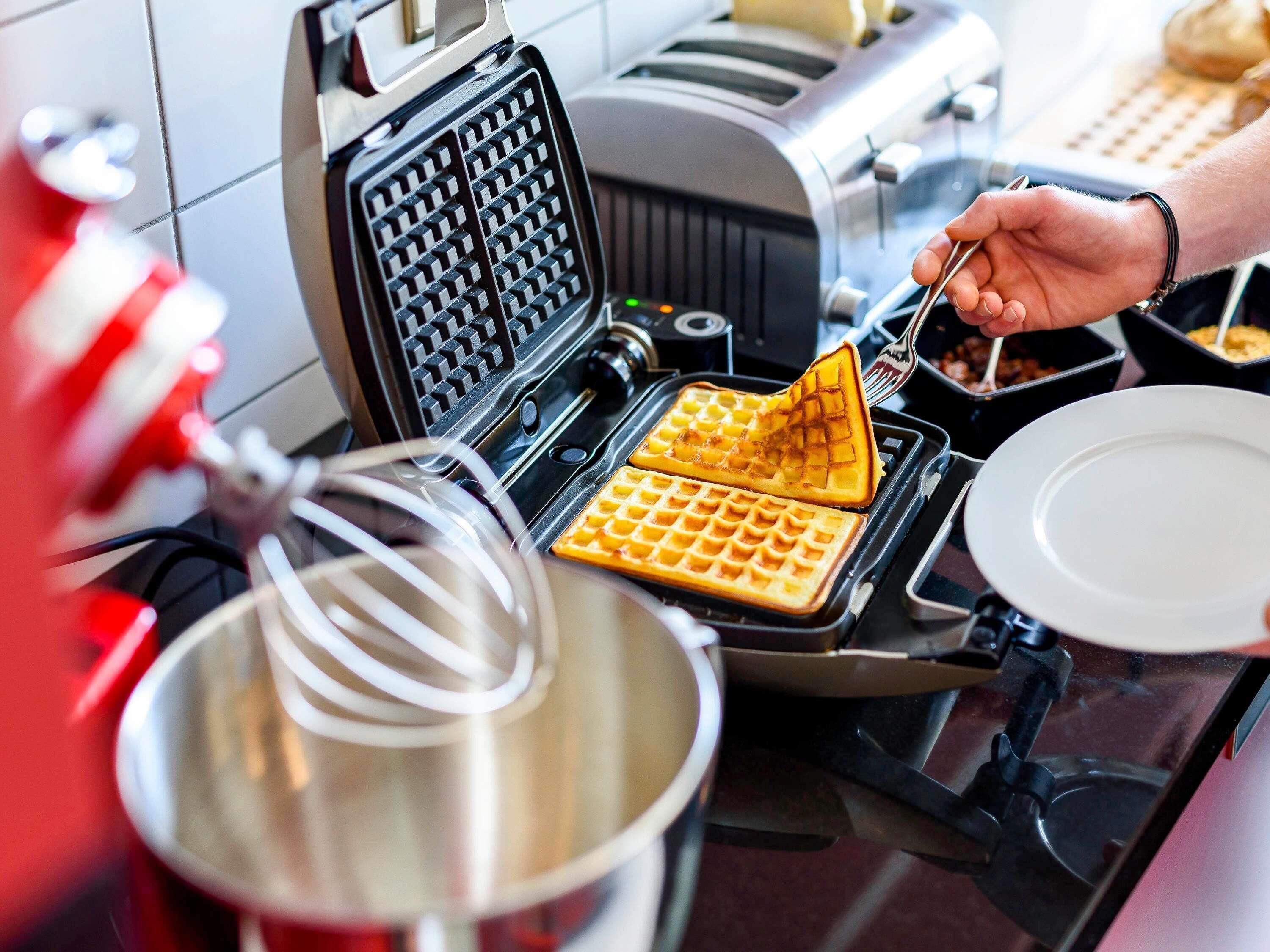 Una máquina para hacer gofres con gofres siendo retirados, un bol para mezclar y un plato sobre una encimera de cocina.