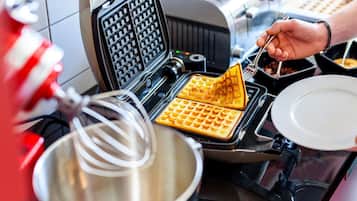 Una máquina para hacer gofres con gofres siendo retirados, un bol para mezclar y un plato sobre una encimera de cocina.
