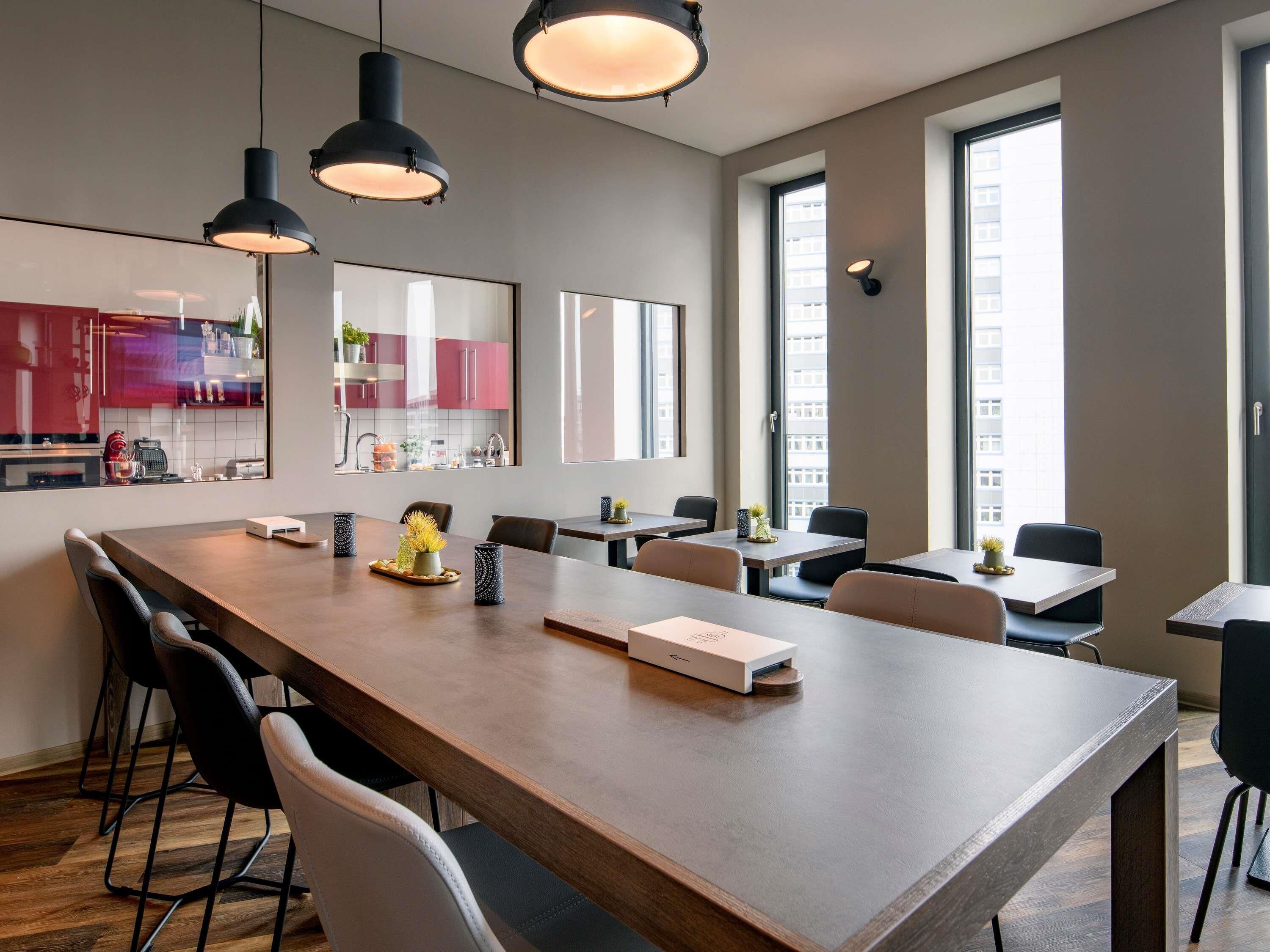Un comedor moderno con una mesa larga, varias sillas, iluminación colgante y amplias ventanas que dejan entrar luz natural.