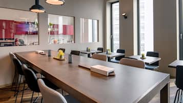 Un comedor moderno con una mesa larga, varias sillas, iluminación colgante y amplias ventanas que dejan entrar luz natural.