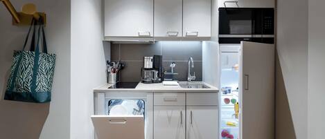 A compact kitchen with white cabinets, a built-in microwave, a dishwasher, and a refrigerator.