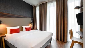Una habitación de hotel con una cama grande, un escritorio, una silla, un televisor y cortinas.