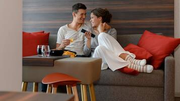 Un salon moderne avec un canapé gris, des coussins rouges, une petite table avec des verres et des en-cas, et une chaise en bois.
