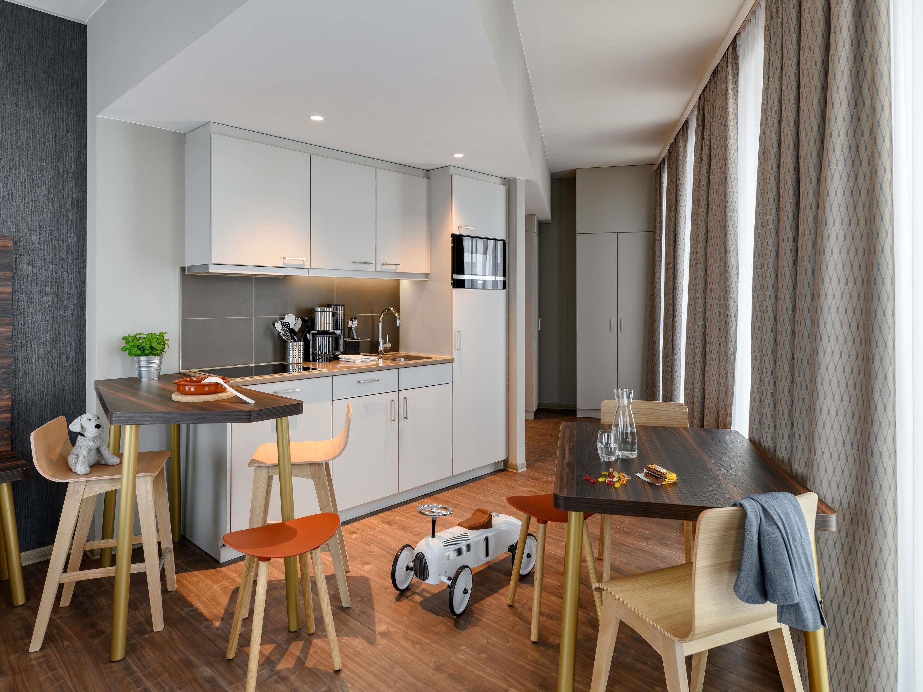 A modern kitchen with white cabinets, a dining area with wooden chairs, and a small toy car on the floor.