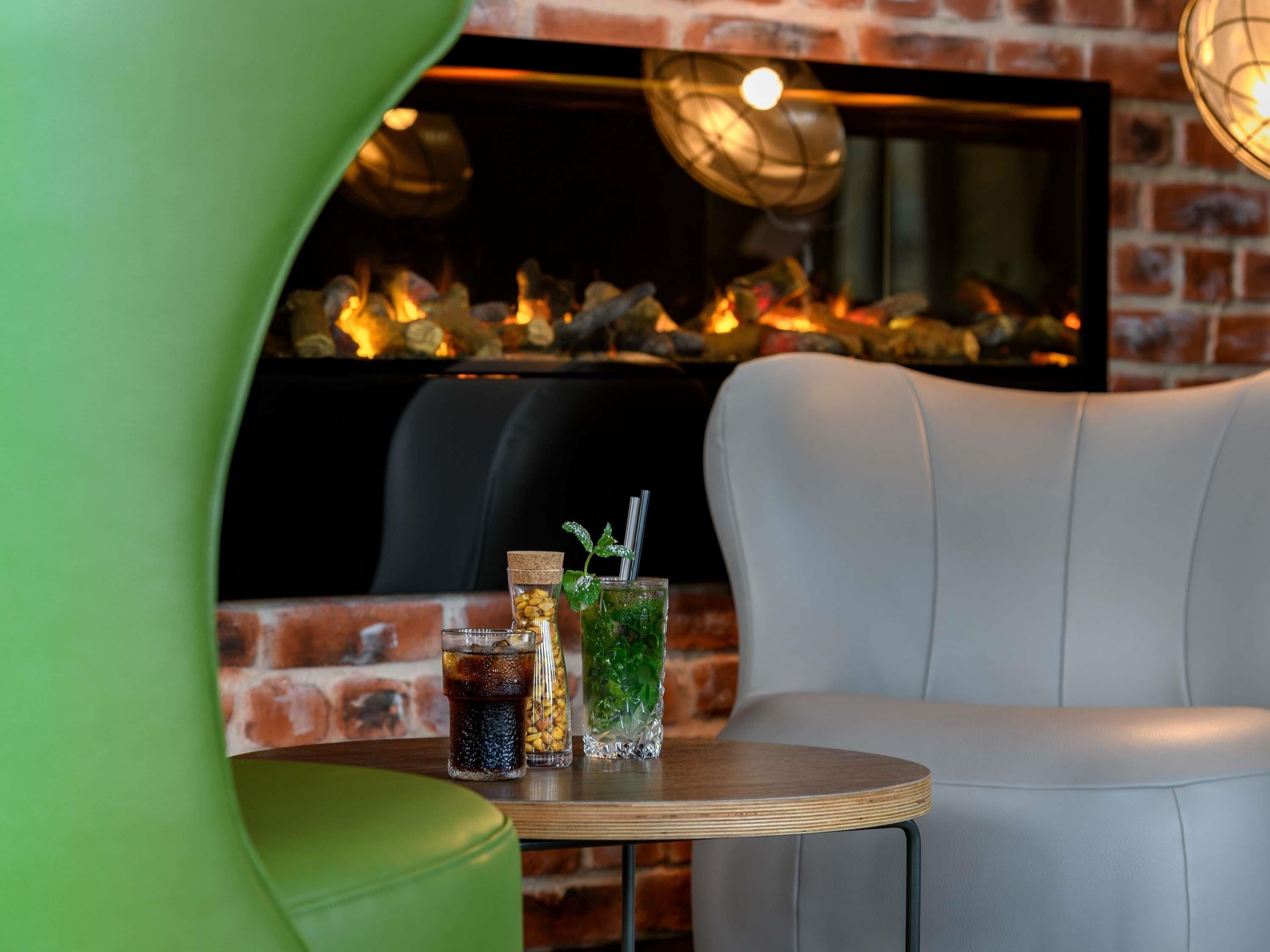 A cozy seating area with a table featuring two drinks and a fireplace in the background.
