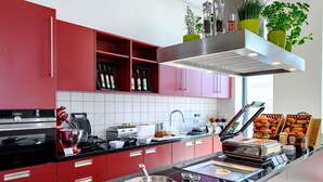 Una cocina moderna con armarios rojos, encimera negra, horno empotrado, máquina de café y barra desayunadora con distintos alimentos.