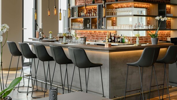 Cocina moderna con barra, destacando una pared de ladrillo, lámparas colgantes y taburetes de bar.