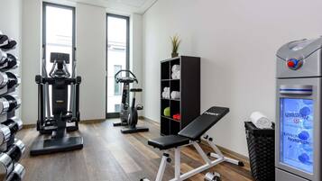 Ein Fitnessraum mit Trainingsgeräten, einer Bank, Kurzhanteln und einem Wasserspender.