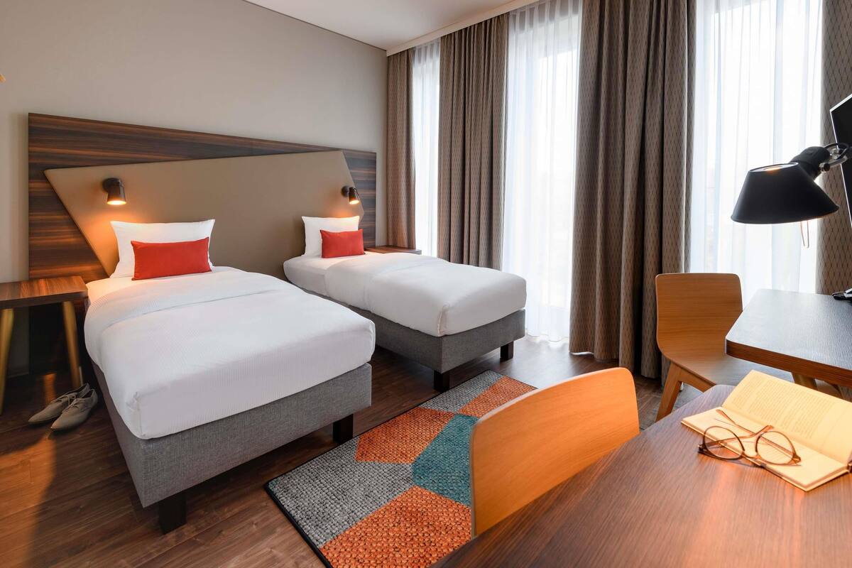 Ein Hotelzimmer mit zwei Betten, einem Schreibtisch, einem Stuhl und einer Lampe.
