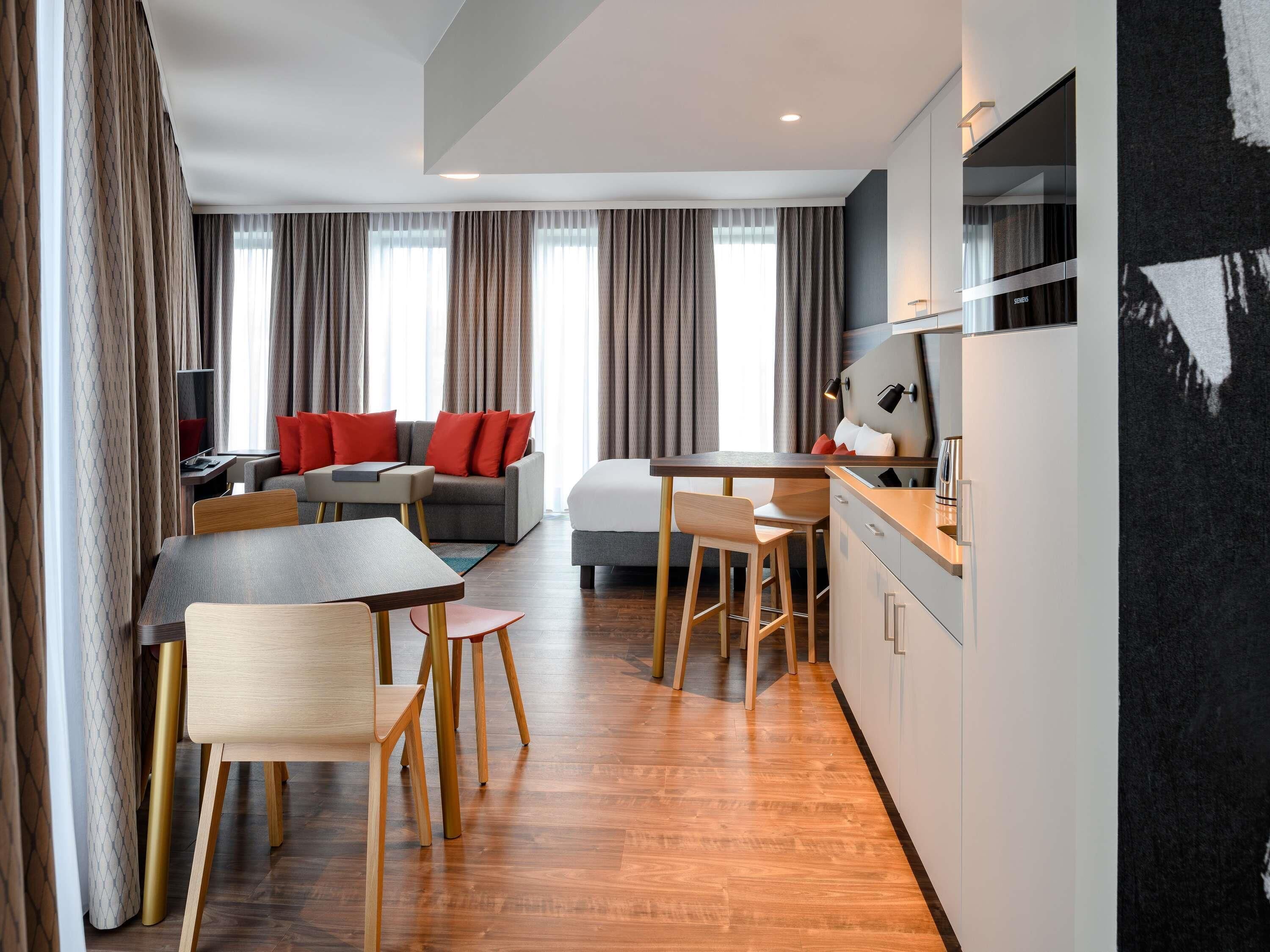 Una habitación de hotel moderna con comedor, sofá, cama y kitchenette.