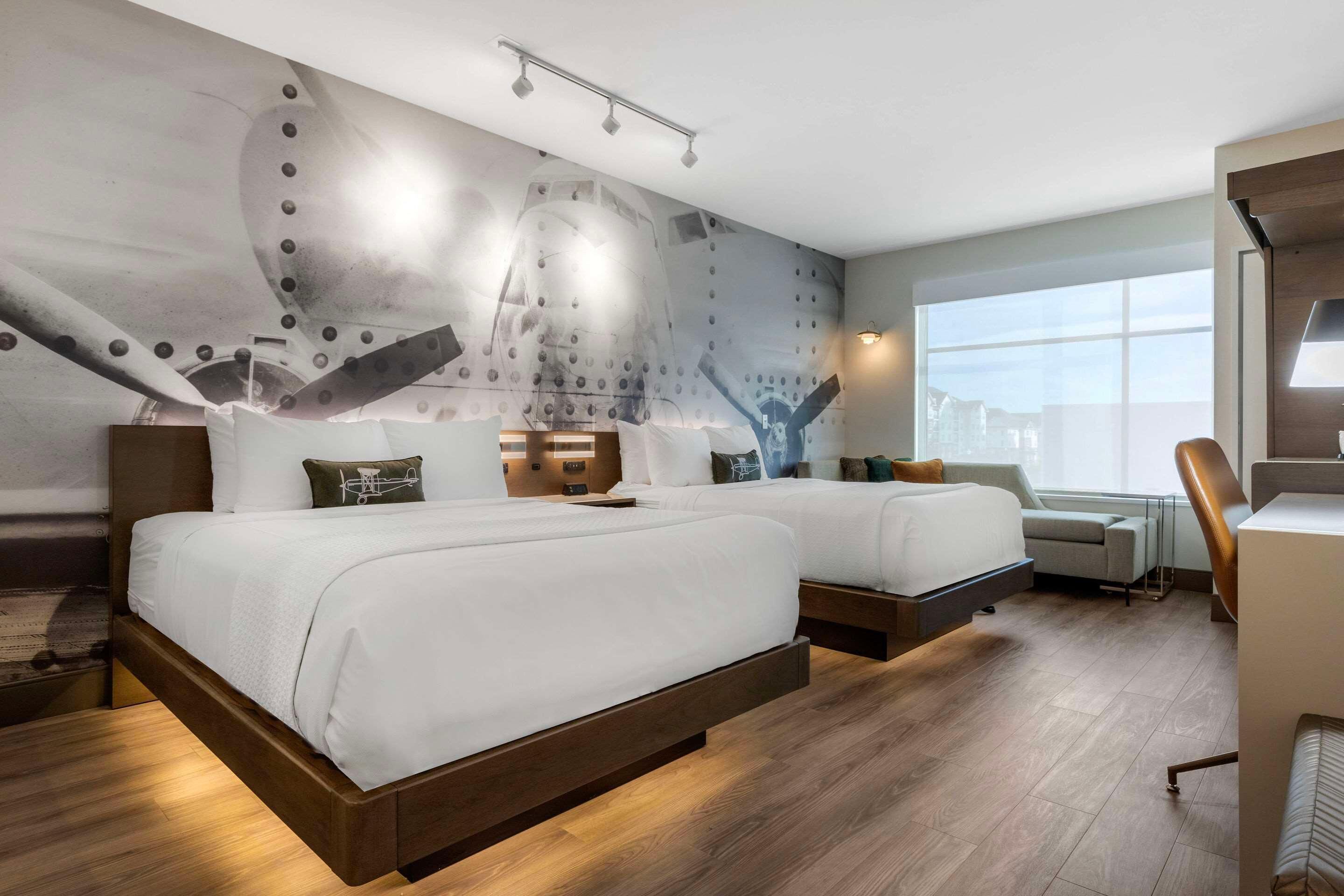 A hotel room with two beds, a desk, a chair, and a large window.