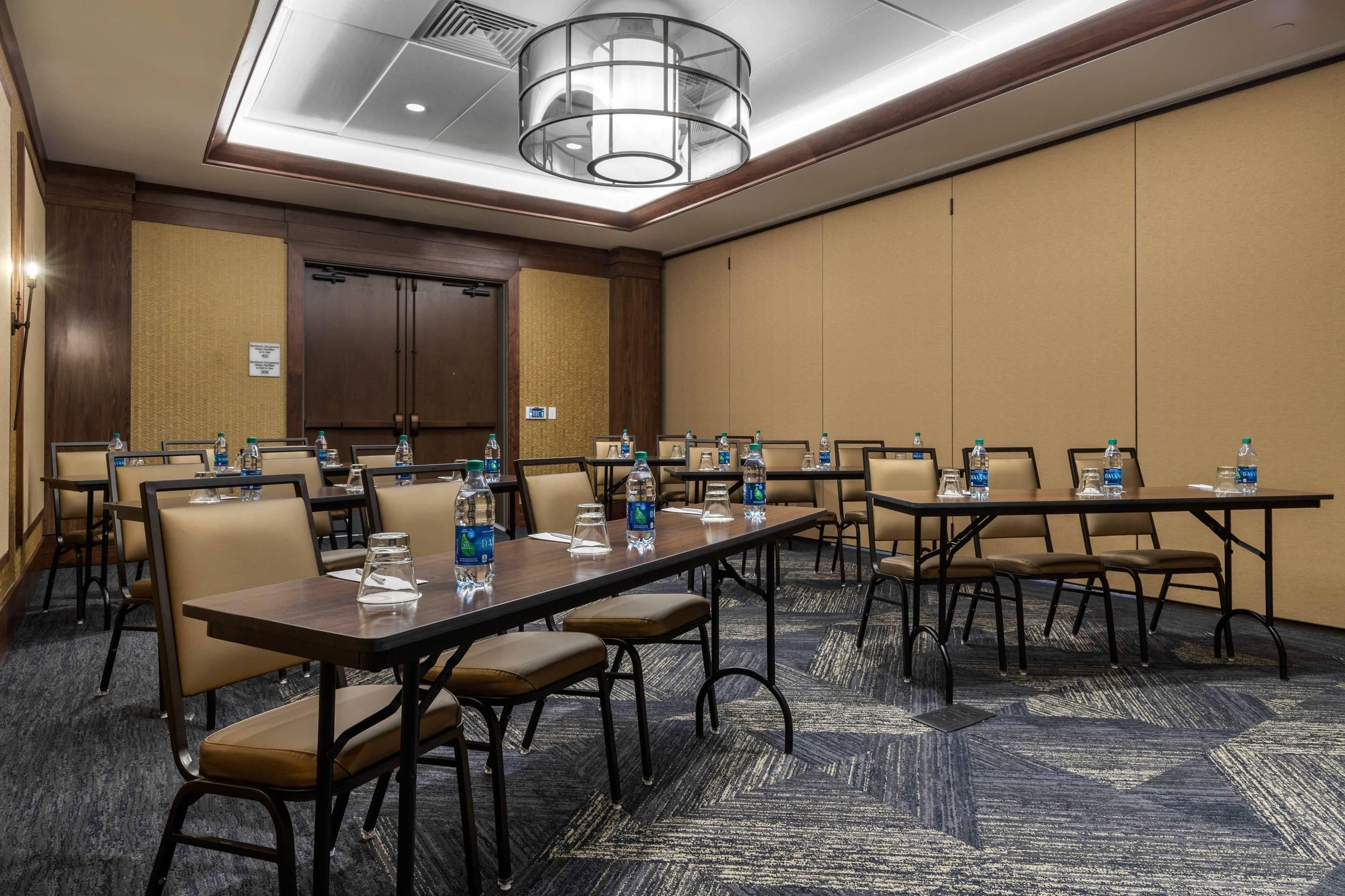 A conference room with multiple tables and chairs, equipped with water bottles and glasses, and a large chandelier.