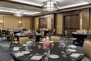 Un salón de conferencias con mesas redondas dispuestas para comer, equipado con copas, cubiertos y velas.