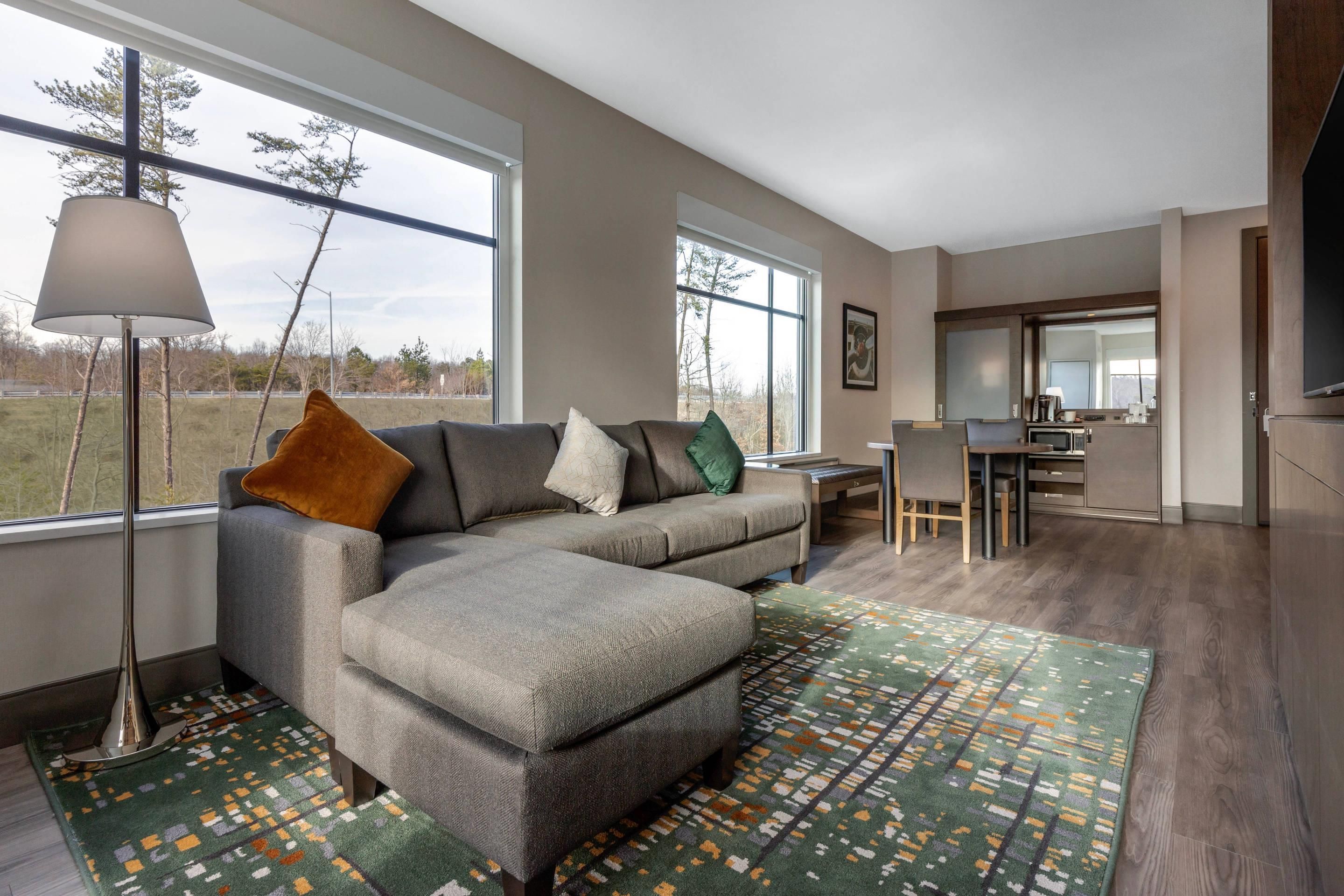 A modern living room with a grey sectional sofa, a patterned rug, and a dining area with a table and chairs.