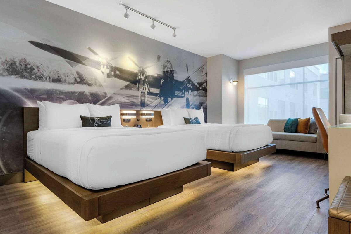 A modern hotel room with a large bed, a sofa, and a mural on the wall.