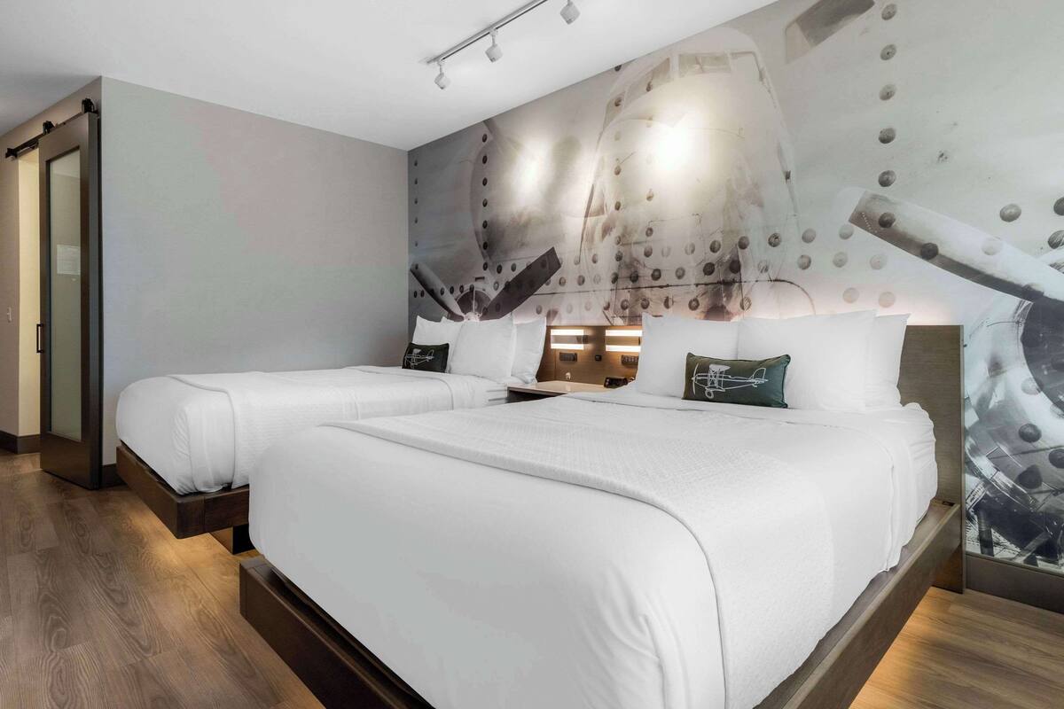 A modern hotel room with two beds, a large abstract mural on the wall, and a wooden floor.