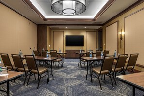 Un salón de conferencias con una gran pantalla plana, varias mesas con sillas y botellas de agua en cada una.