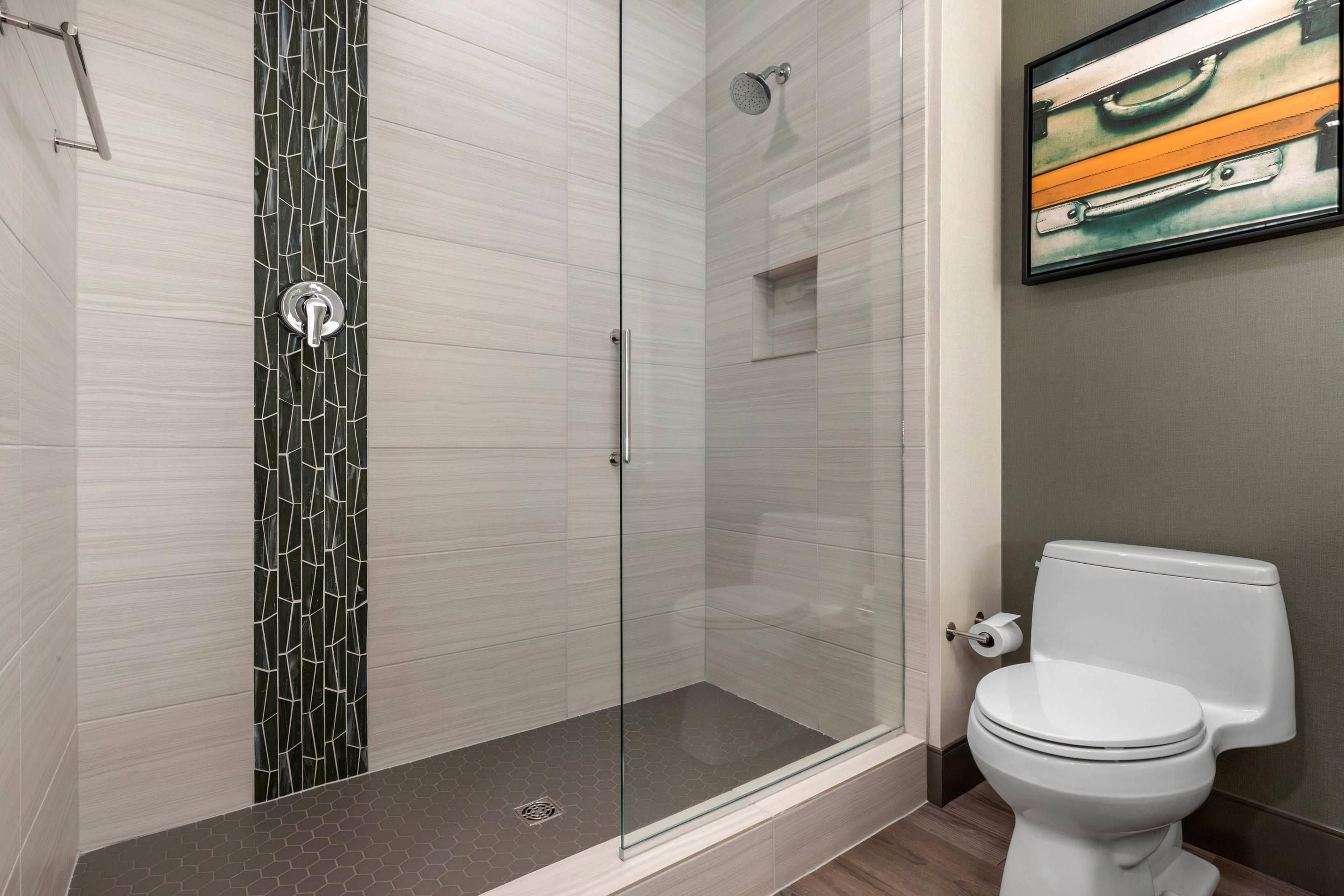 Une salle de bain moderne avec une douche à parois de verre, des toilettes et un tableau encadré au mur.