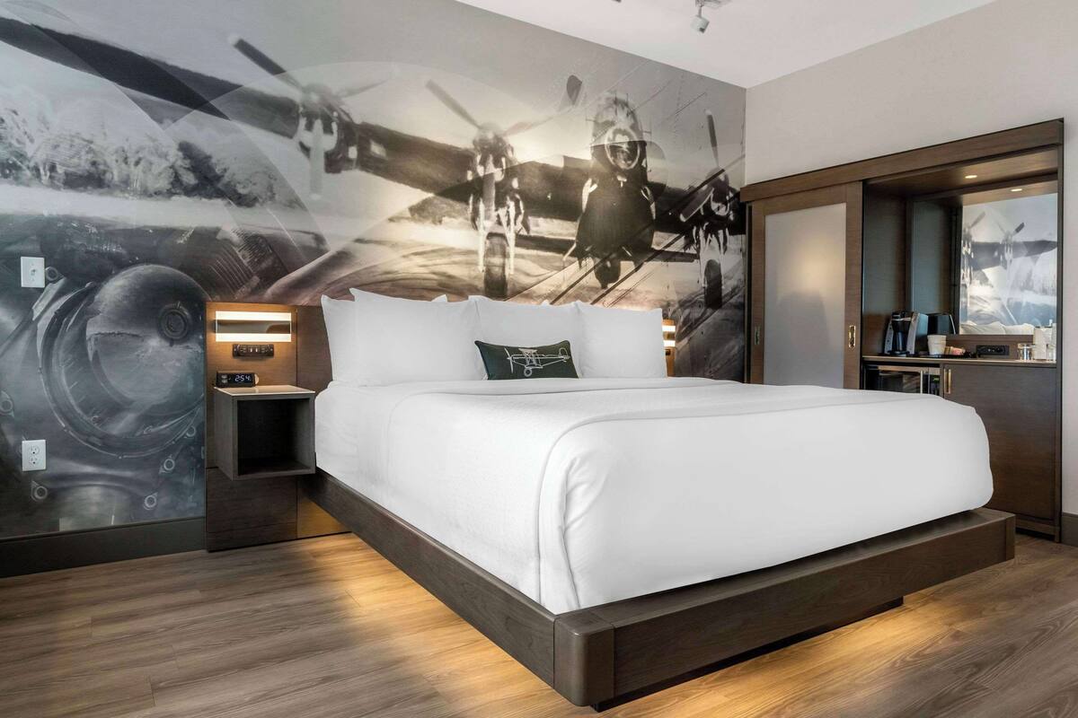 A modern hotel room with a large bed, a nightstand, a built-in wardrobe, and a wall mural of vintage aircraft.