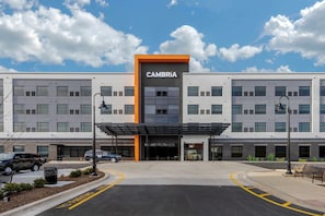 Un edificio moderno con un letrero llamativo de CAMBRIA, una entrada techada y un estacionamiento con líneas amarillas.