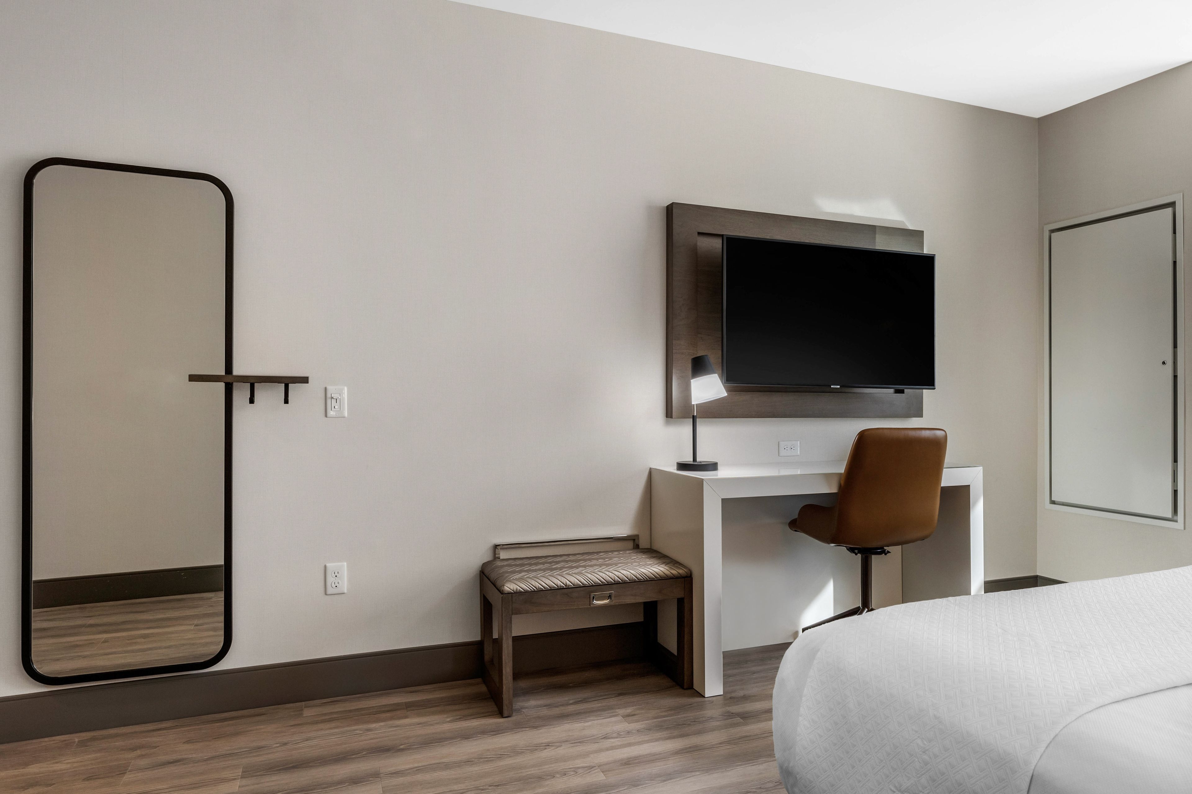 Camera d'albergo con un letto, una scrivania con una sedia, una televisione, uno sgabello e un grande specchio.